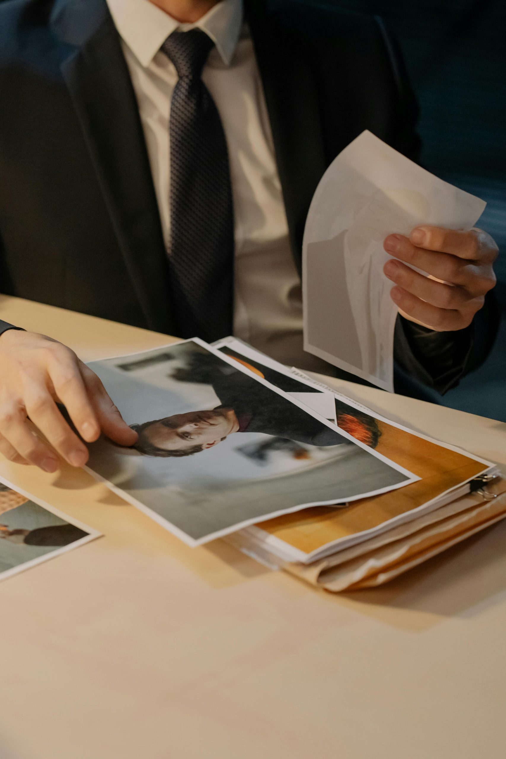 Man in suit analyzing photographs on a desk, suggesting investigation work.