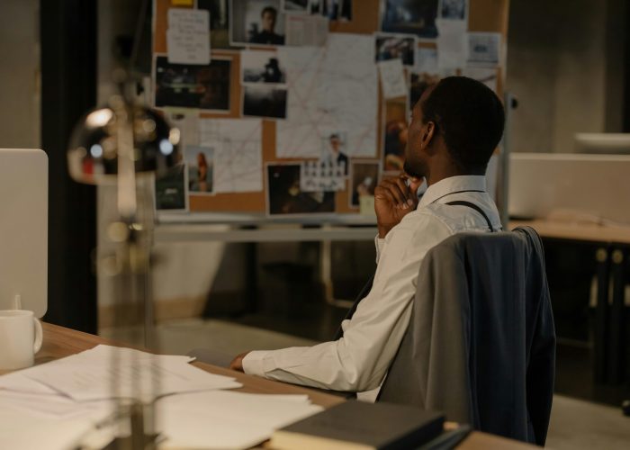 Detective in thought examining evidence board in a dimly lit office environment.